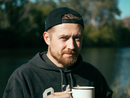 Young man drinking coffee from a white cup. Camping, tourism