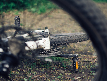 A dirty bike lies on the ground. The details are close-up, the wheels are dirty from a trip in bad weatherの写真素材