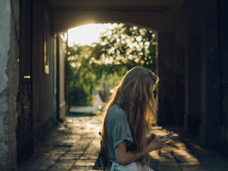 Red-haired young girl in the rays of sunset writes a message in the phone.の写真素材