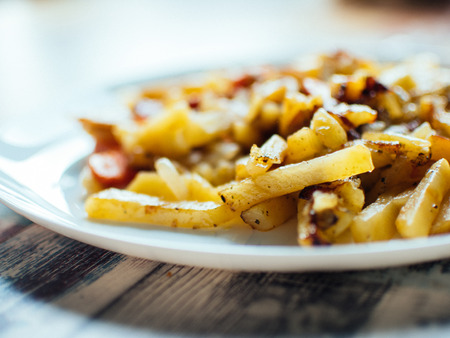 Spicy fried potatoes with herbs and spices served in white plate. Shallow depth of field photographの写真素材