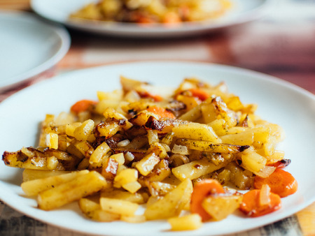 Spicy fried potatoes with herbs and spices served in white plate. Shallow depth of field photograph