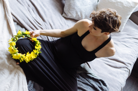Future mother sits on a bed. The pregnant woman in a black dress.の写真素材