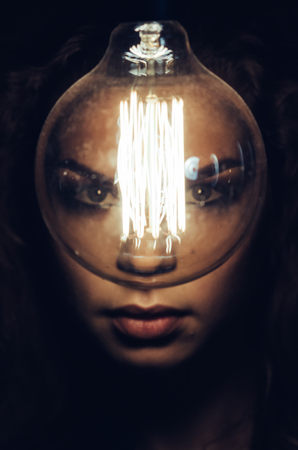 Mysterious photo of woman with light bulb. Portrait in the dark. Dangerous girl.