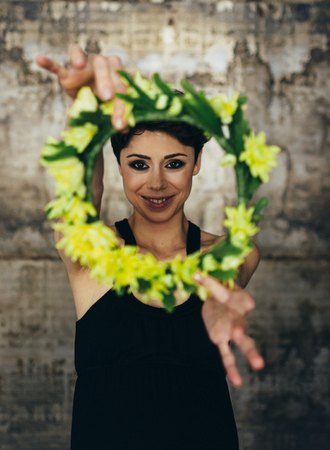 Portrait of a charming young lady with a flower crown, in a retro blouse. The girl looking pensively at the camera on the grey backgroundの写真素材