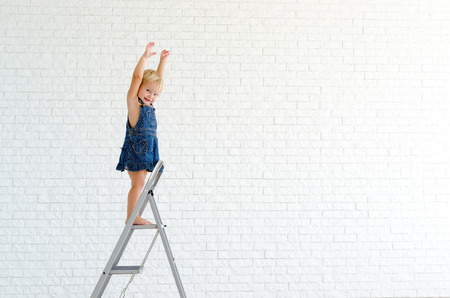 Little girl at the ladder, with the white brick wall on background.の写真素材