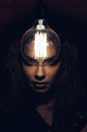 Mysterious photo of woman with light bulb. Portrait in the dark. Dangerous girl.の写真素材