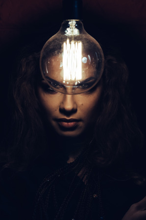Mysterious photo of woman with light bulb. Portrait in the dark. Dangerous girl.の写真素材