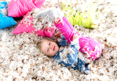 A beautiful child enjoying life. Child jump on bed and fught with pillowの写真素材