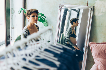 shopping, fashion, clothes, style and pregnancy concept - happy woman trying coat on in mall or clothing store.の写真素材