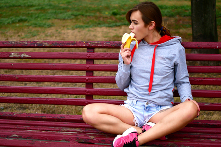 A young sweet girl is very seductive eating a banana. A sports woman watches her food.の写真素材