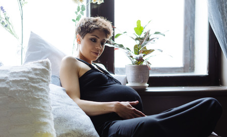 Future mother sits on a bed. The pregnant woman in a black dress.の写真素材