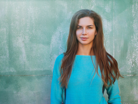 Portrait of a beautiful young caucasian girl. A woman in a blue sweater against the backdrop of a blue wall, a place for text.の写真素材