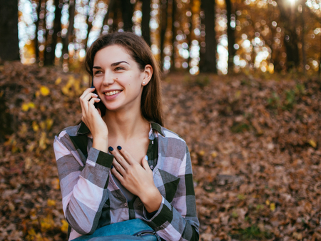 Young caucasian girl talking on a mobile phone on the background of the autumn forest.の写真素材