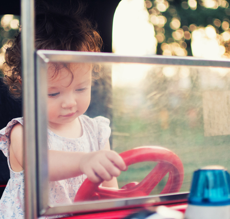 A child behind the wheel of a toy car. Toddler girl in the carousel amusement park.