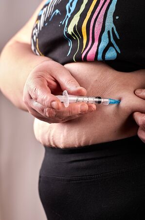 Woman with syringe make a subcutaneous abdomen injection of insulin to her belly - diabetes conceptの写真素材