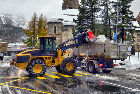 Snow cleaning tractor snow-removal machine loading pile of snow on a dump truck. Snow plow outdoors...