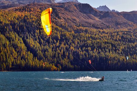 Mountain landscape with a lot of kite surfers and windsurfers moving in a lake. They use the wind to move their boards on the waterの写真素材
