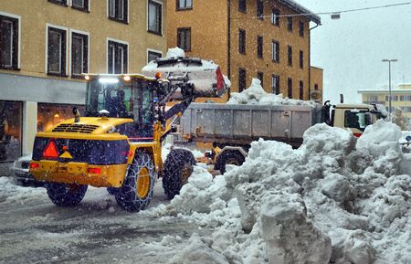 Snow cleaning tractor snow-removal machine loading pile of snow on a dump truck. Snow plow outdoors...