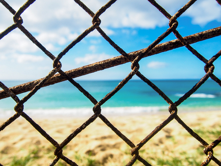 Closeup photo of a rusty old chain link fence with a beach in the background near Makaha Hawaii.の写真素材