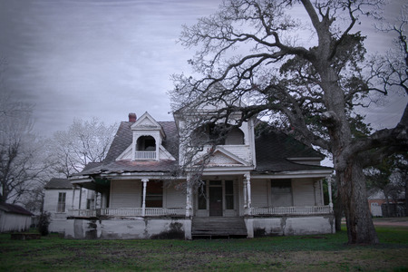 Spooky old haunted house with a dead tree in the yard in rural Texas.のeditorial素材
