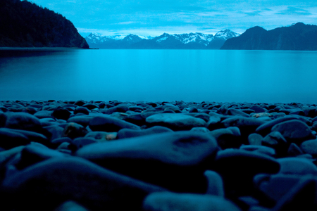 Smooth beach stones on the shore in the foreground of a landscape photo overlooking the ocean and mountains in Seward Alaska at midnight.の写真素材