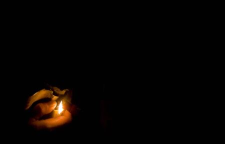 A hand using a lighter to light a fire with a black background.の写真素材
