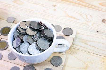 coins in a white coffee cup is placed on a wooden table and around a cupの写真素材