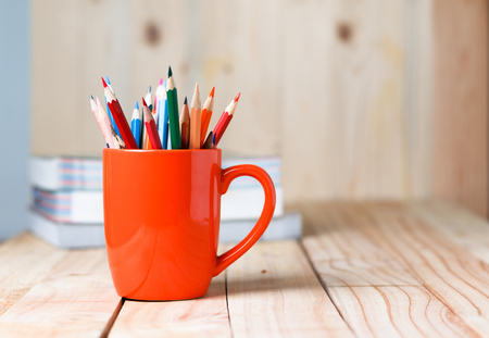 color pencils in a glass on an orange wooden boardの写真素材