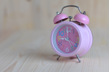 Pink alarm clock place on the wooden table and wood background. Alarm clock is old and colourful numbers. Select focus shallow depth of field and blurred backgroundの写真素材