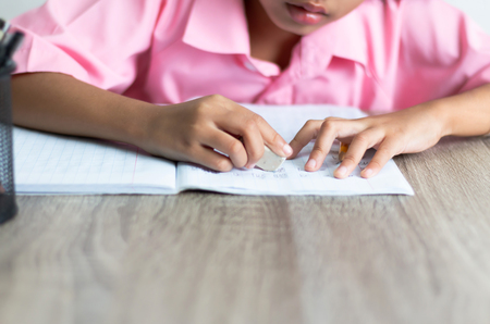 Children use a eraser is deleting words. Close up the little girl is doing homework on the wooden table.の写真素材