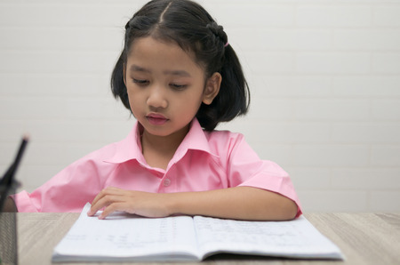 The little girl is doing homework. Children looking a notebook on the wooden table. Select focus shallow depth of field.の写真素材