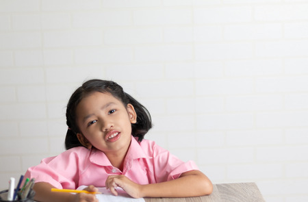 The little girl is doing homework. Children use a yellow pencil is writing a notebook on the wooden table. Select focus shallow depth of field with copy space.の写真素材