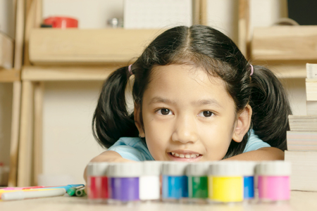 Little girl looking forward and smilling. Color group and book on the desk. Back to school.