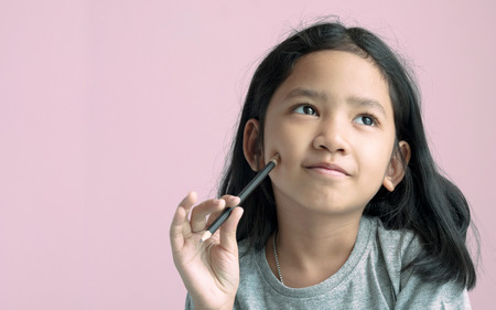 Asian girl holding a pencil and thinking something with pink background.の写真素材