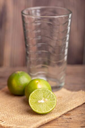Close up a half of the green lime place on the woven sack and blerred empty glass in a kitchen. Select focus shallow depth of field. Lemon is a kind of fruit. The result is very sour. Organized in the genus Orange and green when ripe it is yellow with thin skin, inside the petals are very moist, divided into valuable fruit.の写真素材