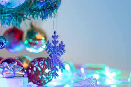 Close up snowflake and christmas balls hanging on the branch of the pine. Christmas decorations to celebrate the holiday season. Gift boxes below the tree and neon light with bokeh reflection. Select focus shallow depth of field and blurred backgrounds with copy space.の写真素材