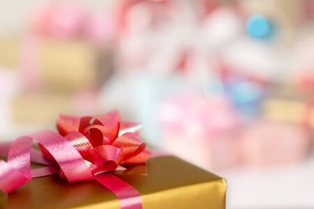 Close up a gold gift box tied with a pink ribbon and a red flower placed on the table. Surprise...