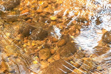 The beautiful ripples in nature on the river flowing over stones in the summer sunshine. Rocks under...