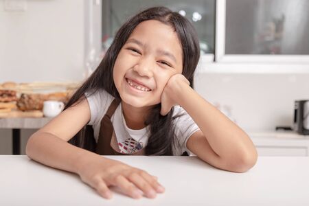 Asian little girl smiling saw her broken tooth on a white cooking table in the kitchen with happiness.の写真素材