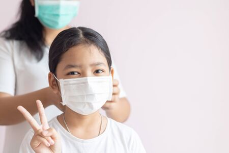 Asian little girls wear medical protective masks and raise 2 fingers. Prevent the spread of influenza, Coronavirus or COVID-19 and pm 2.5 illness.の写真素材