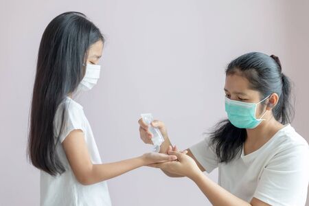 Little girl and a woman wear a protective medical mask. Hands of the mother squeeze the alcohol gel in the tube onto the palm of the daughter to clean. The protection for the Coronavirus or COVID-19.の写真素材