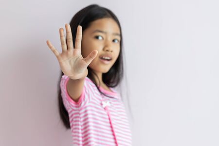 A little Asian girl is wearing a pink dress with a white stripe. The child reaches out to show the sign of stopping out in front. Select focus shallow depth of field and blurred background.の写真素材