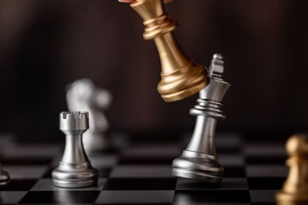 hand holding gold king attack silver leader in game on the chessboardの写真素材