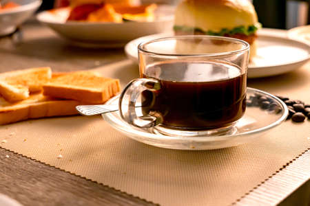 The breakfast and hot black coffee on the wooden table with a sunbeam in the morning.の写真素材