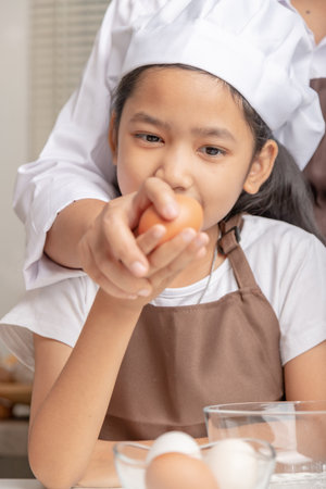 Mother and daughter are helping to collect eggs on the table for cooking. The little asian girt looking an egg in a hand. Select focus shallow depth of field.の写真素材