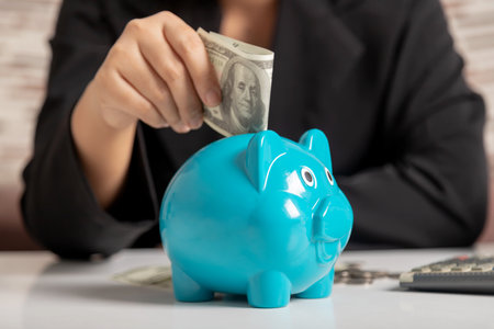 Close-up a businesswoman hand putting money bank note dollar into a piggy. Saving money wealth and financial concept.の写真素材