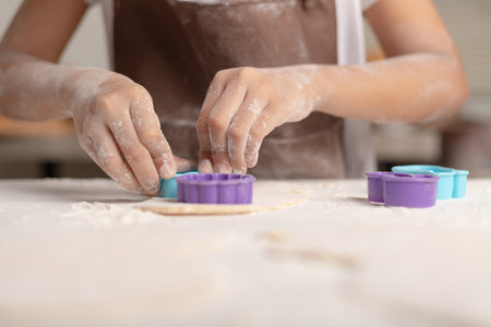 Close-up A little Asian girl is wearing a brown apron using a blue mold to cut the dough for making cookies in the kitchen.の写真素材