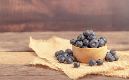 fresh blueberry in a wood bowl and heap on the old sack wiht brown wooden table.の写真素材
