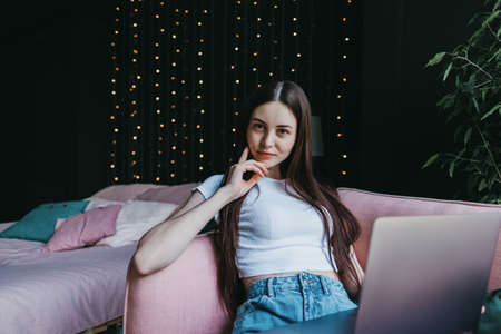 Portrait of successful female freelance worker, sitting on pink sofa and using a laptop computer.の写真素材