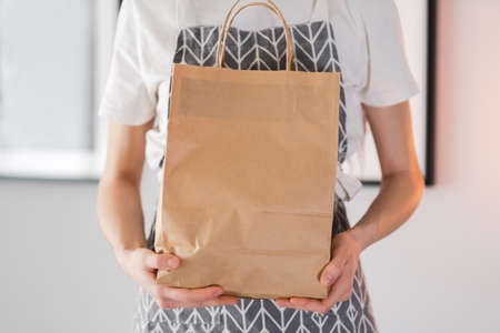 Woman holds craft eco shopping bag in hands, take away. Delivery food, mock up. High quality photo